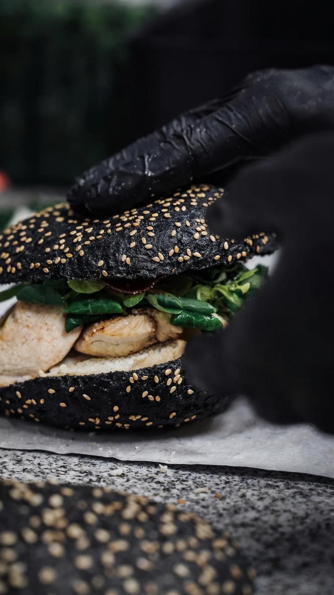 Assemblage burger au pain noir aux graines de sesame, mains gantees noires